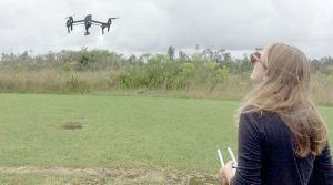  A student controls a drone rising above a grassy field.