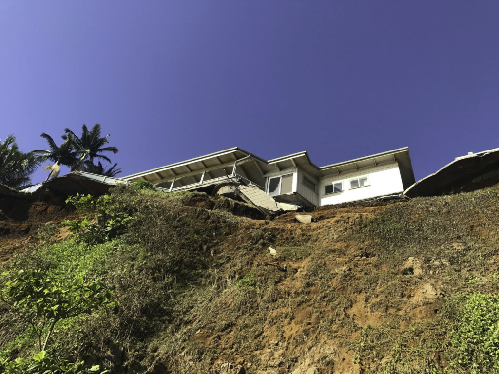 A home precariously near an eroding sea cliff with some damage to the back patio where it looks like some parts of the structure has fallen.