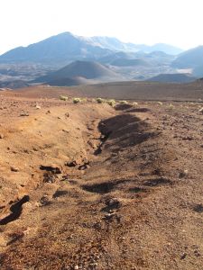 An eroded gully stretches along an open plain to cinder cones in the background