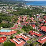 Aerial view of UH Hilo with red roofs and Hilo bay in the background.