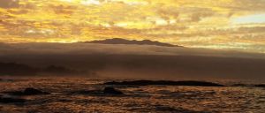 Maunakea from Hilo Bay with layer of cloud in the middle showing the peak popping through the cloud layer at sunset.