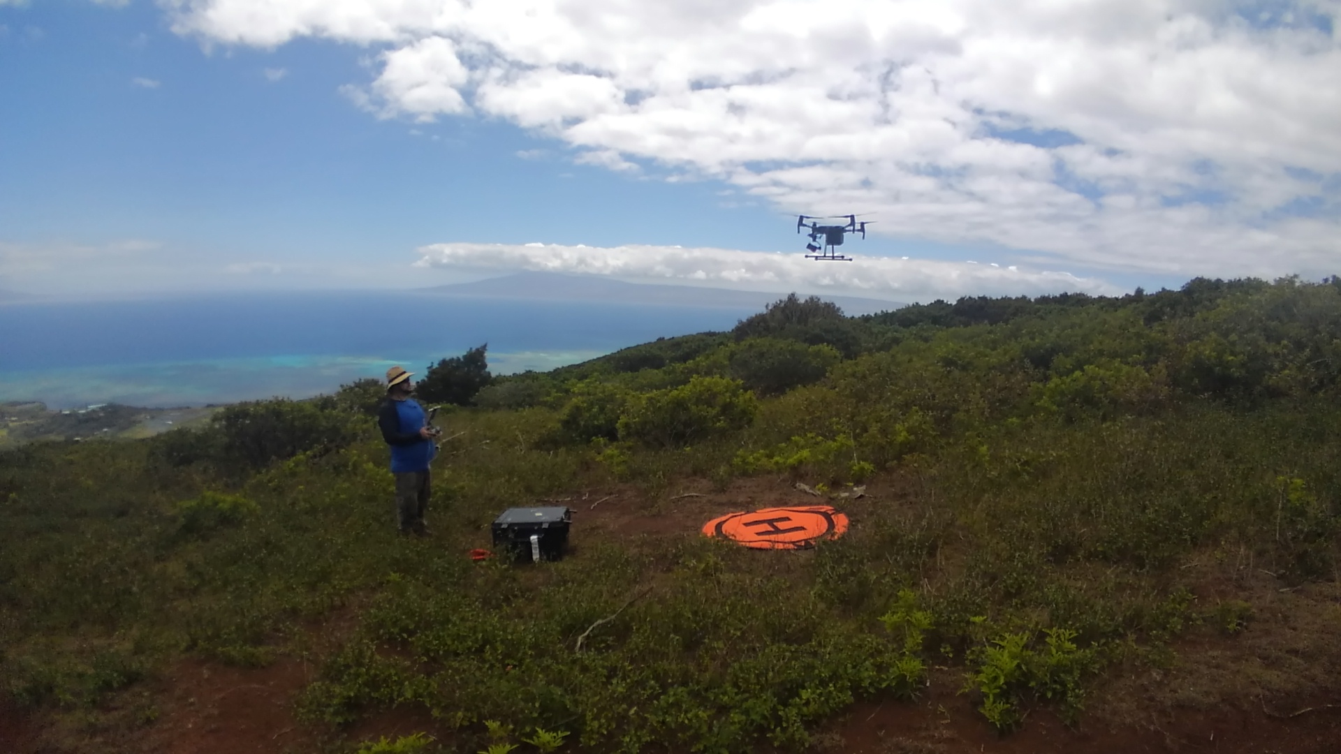 Student controls a drone that has lifted off from an orange landing spot in a scrubby landscape.