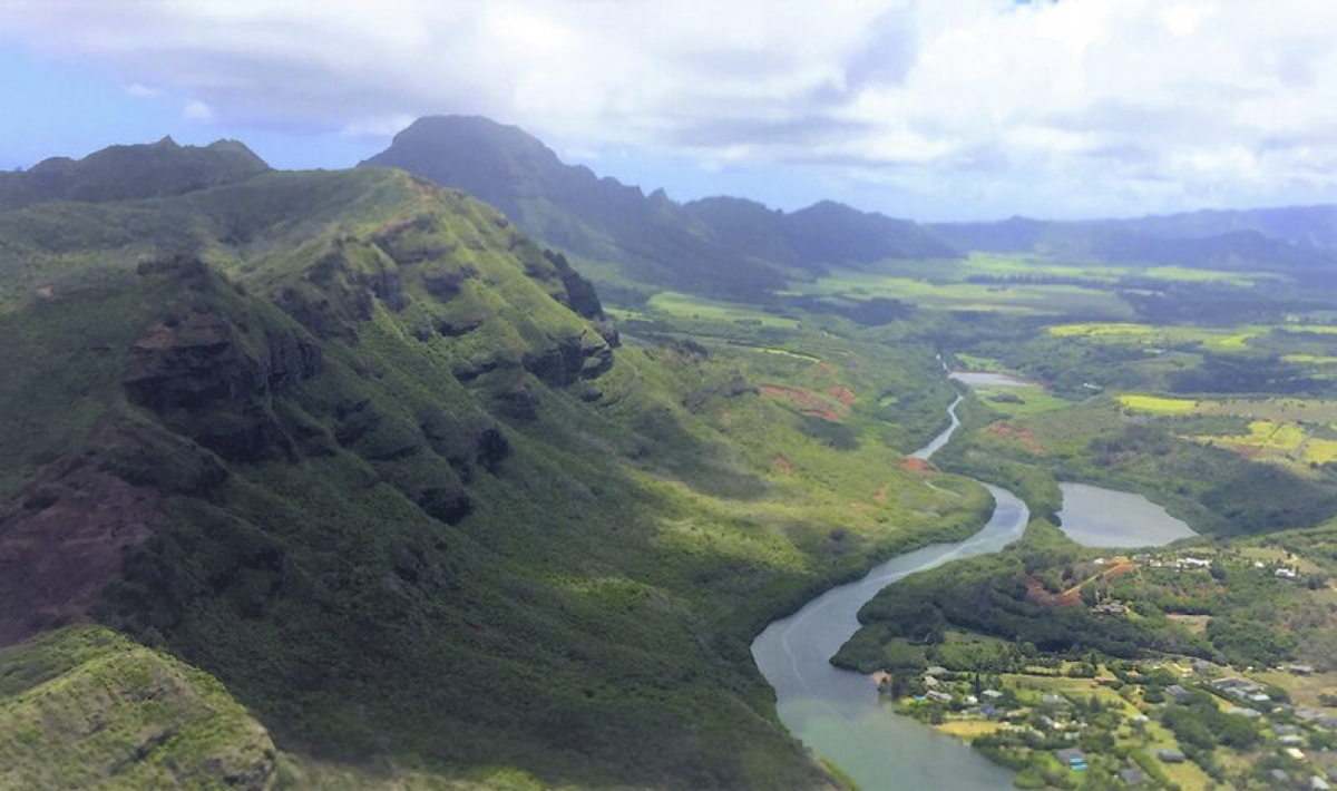 Expansive landscape of green, rocky hills, a river snaking along their base and a fishpond