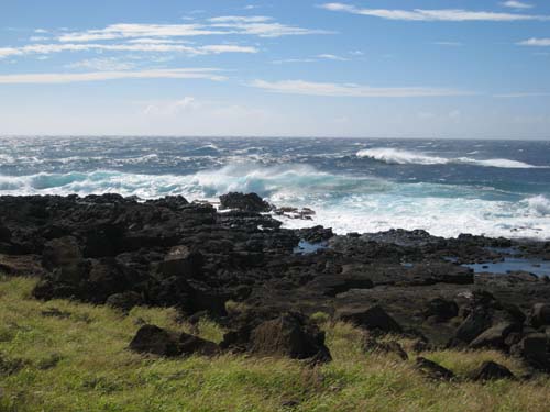 Spume-capped waves crash against a low black basalt rock shoreline