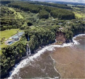Eroding sea cliffs in Hilo with homes right on the cliffside featuring waterfalls and a large landslide with brown water.