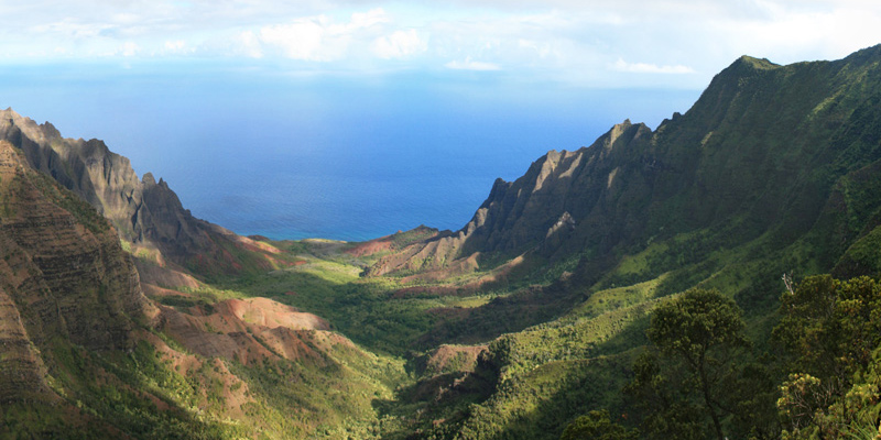 View from the top of a steep, green-sided, u-shaped valley opening onto a blue ocean