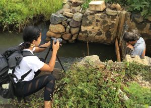 Student photographs someone fixing a sluice gate in a fishpond wall