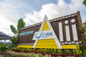 Welcome sign at Our Ocean with many plants in front and made of wood. Has welcome greeting Alii on the background of sign.