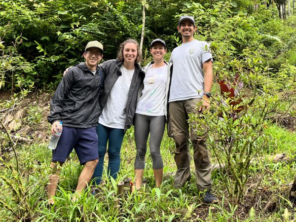 Four students post in front of lush vegetation