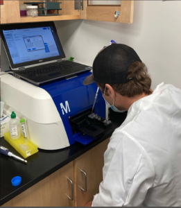 A student holds a pipet as he adds samples to a machine