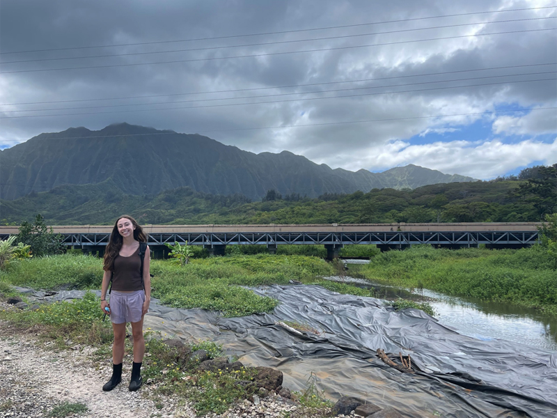 A student stand near a marsh water channel, posing for the camera