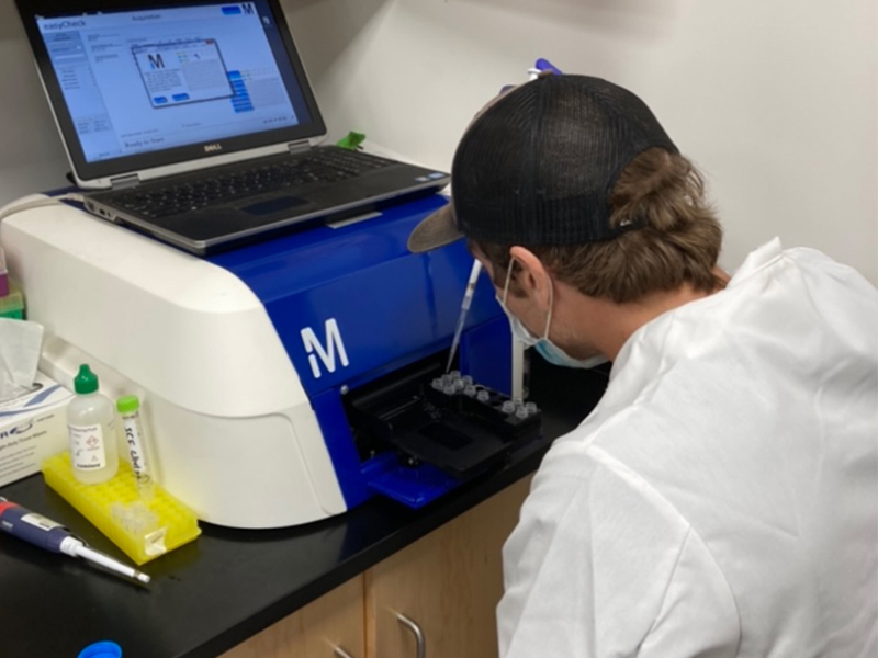 A coated student pipets samples into an analyzer in a lab