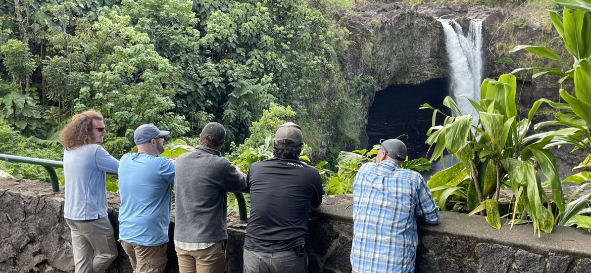 Five men leaning on a side wall and looking at a waterfall