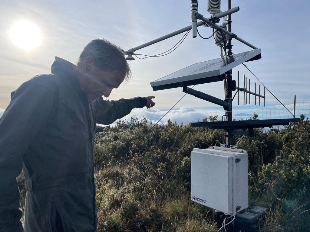 Giambelluca stands near weather station amidst scrub with clouds below and behind