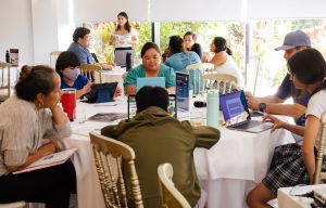 People are seated at round tables and are looking at their electronic devices.