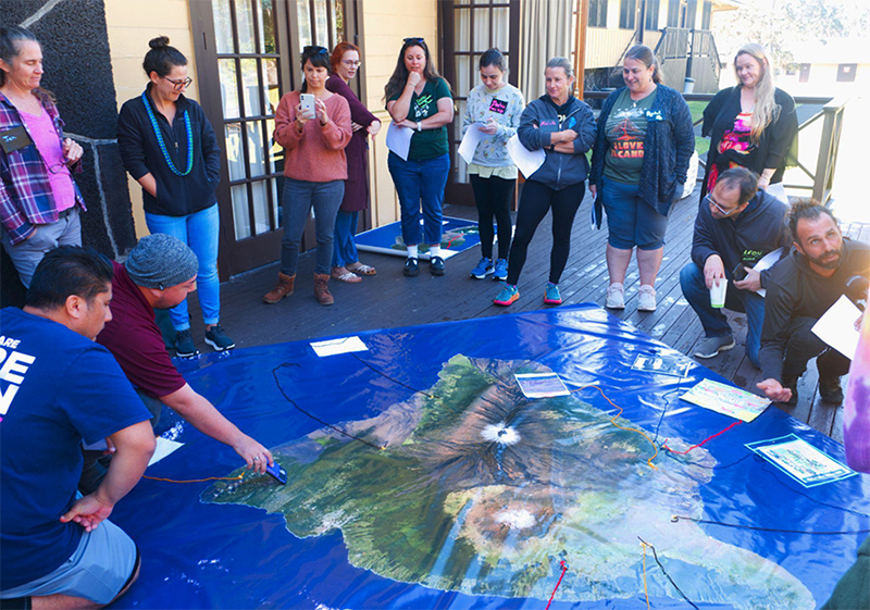 Participants stand around a map of Hawaii Island on the ground as a leader points out Kilauea