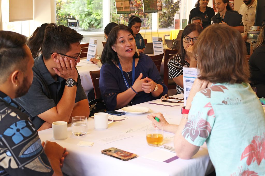 A group of three women and two men are seated at a table, in discussion.