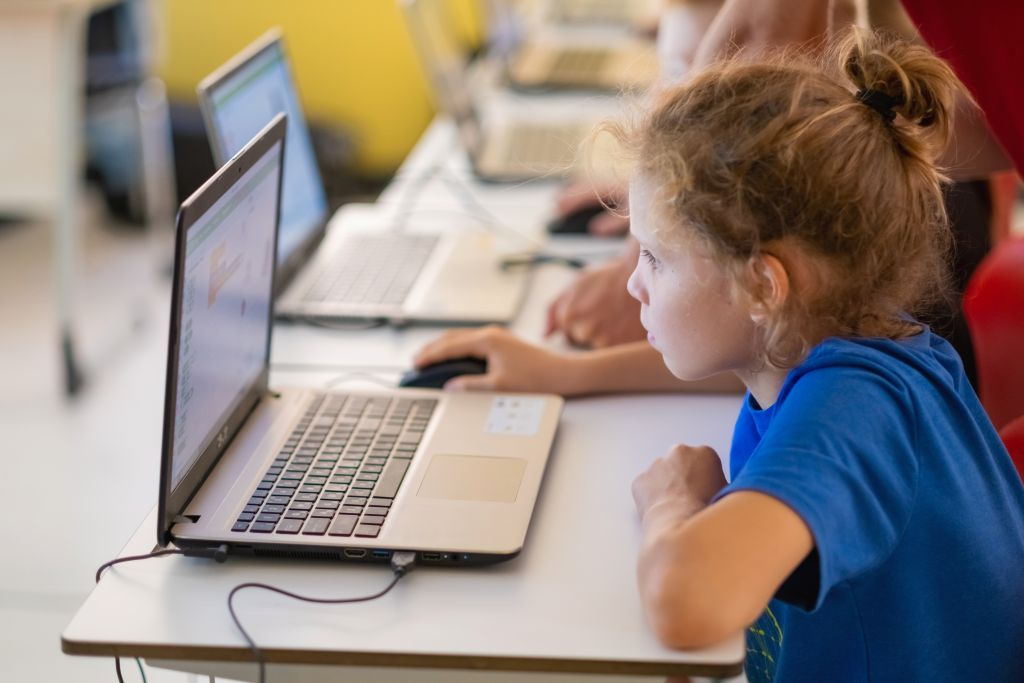 School children using computers in classroom at school.Interracial primary classroom learning to use laptop.