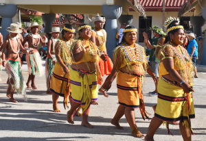 A group of women in cultural Micronesian attire are seen walking in a line. They are followed a group of men, who are also in cultural attire.