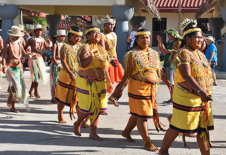 A group of women in cultural Micronesian attire are seen walking in a line. They are followed a group of men, who are also in cultural attire.