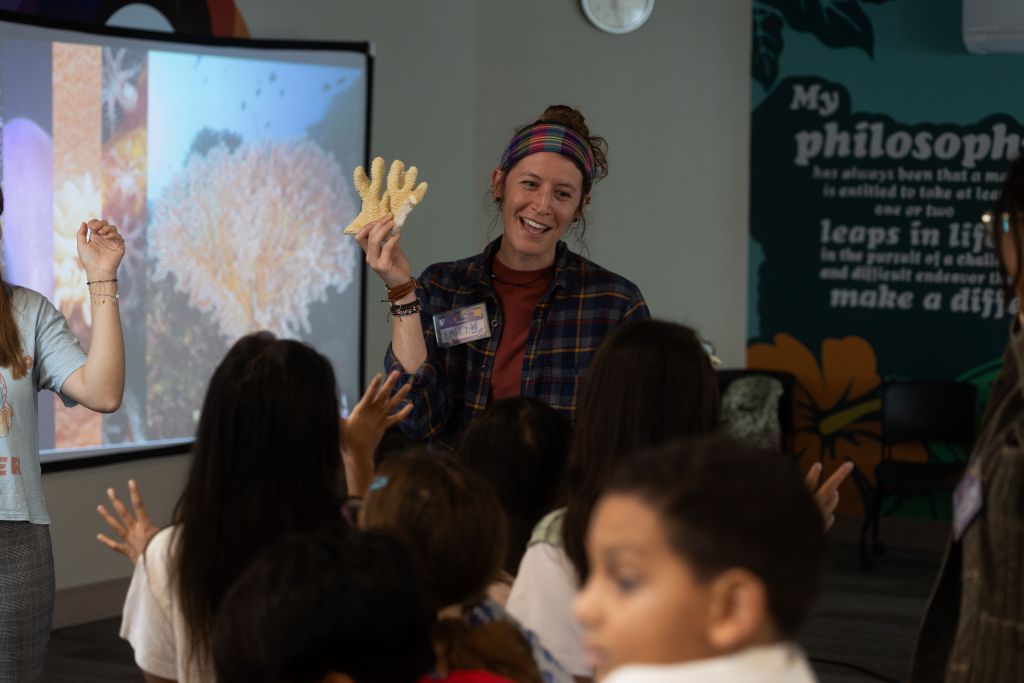 A woman who is holding a piece of coral is seen talking to children