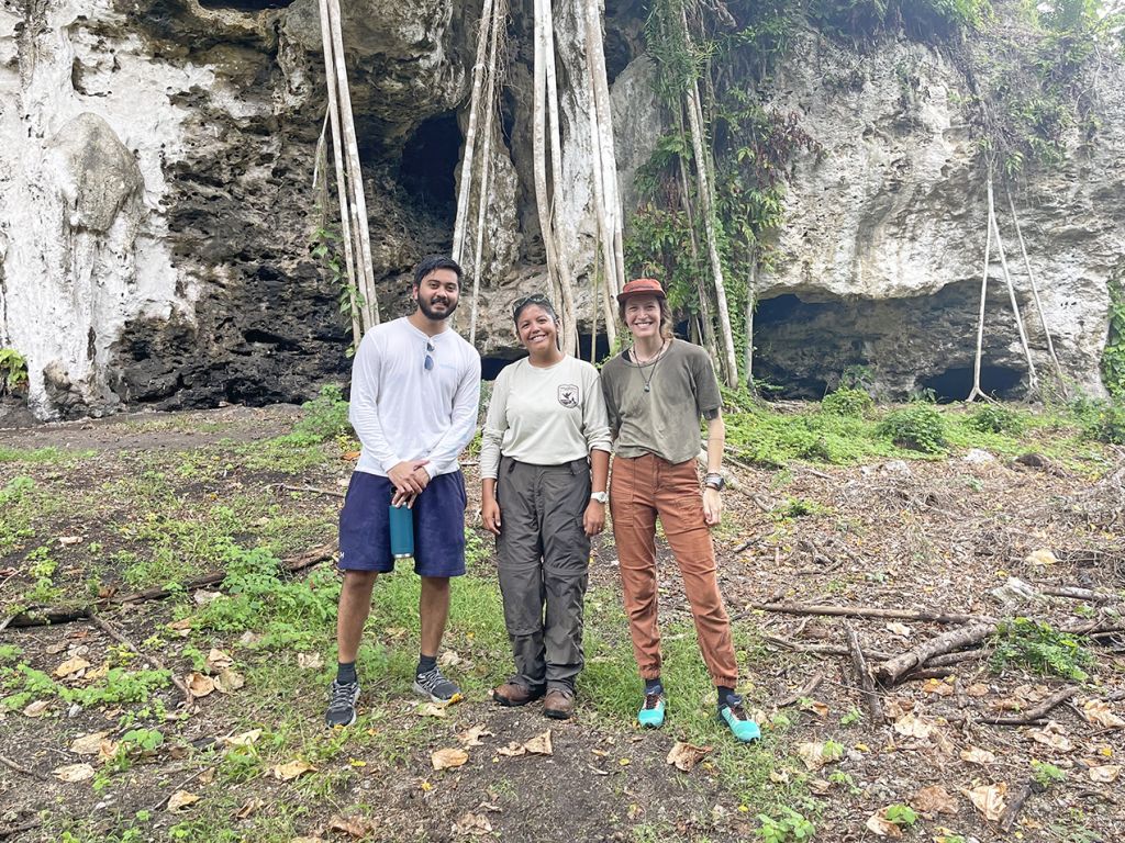 One man and two woman are pictured together in front of a cave opening.