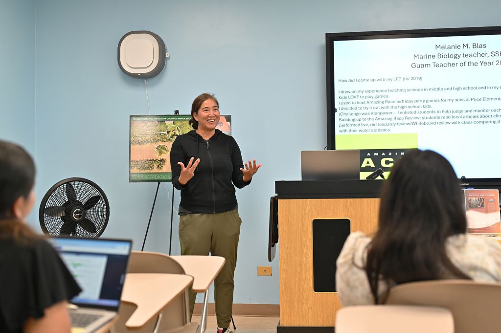 A woman is speaking in front of a classroom.