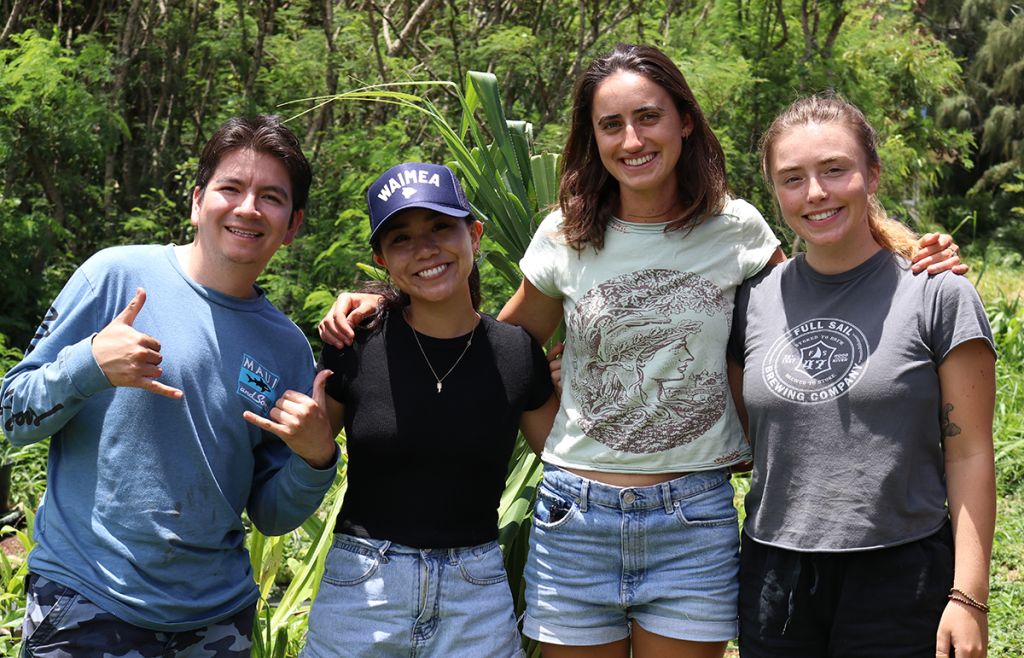 Four smiling students pose for the camera against a background of green plants