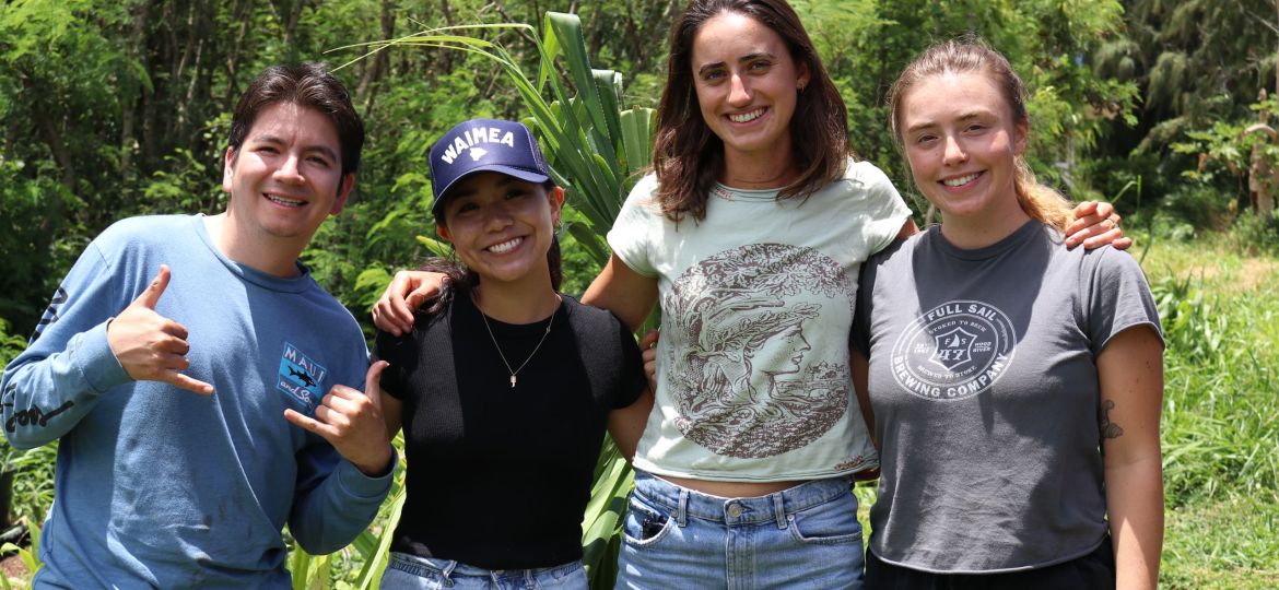 Four students pose, smiling, outdoors with a vegetated background