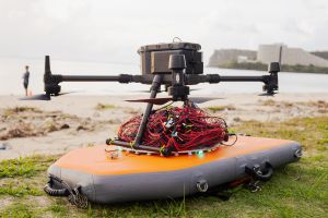 A drone rests over a buoyant device. Under the drone is a coil of wires.