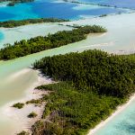 Oblique aerial view of atoll reefs, bright blue and aqua lagoons, and narrow stretches of deep green forests perched on the limited surficial sandbars