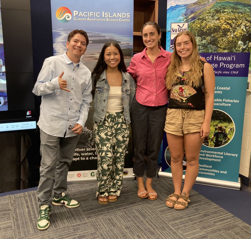 Four smiling students pose in front of a PI-CASC banner