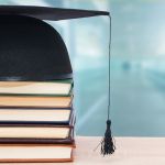 A graduation cap rests atop a stack of books.