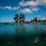 Sean wades in the ocean holding on the floating equiptment.