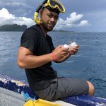 Bryan wearing snorkel on head, sitting off the side of a boat, holding samples.